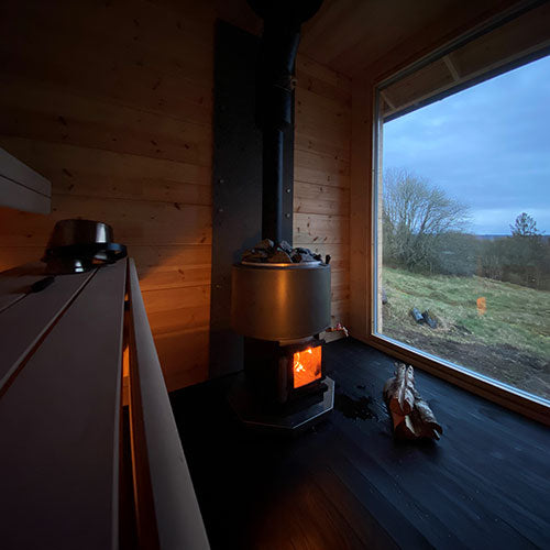 Narvi wood-burning sauna stove inside wooden sauna room with glowing fire and large window view