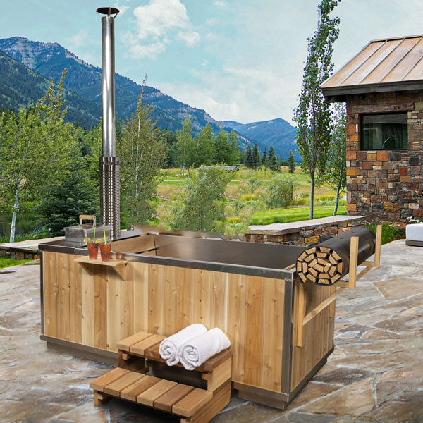 Leisurecraft wood burning hot tub with wooden steps and stacked firewood on stone patio with mountain view